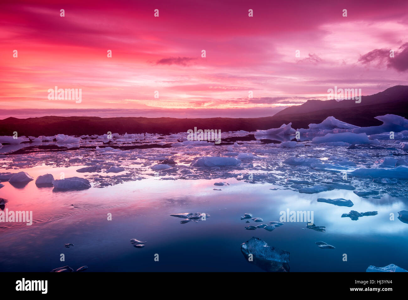 Les icebergs Jokulsarlon glacial lagoon lors d'un rouge vibrant sunrise repose immobile comme il est entouré par l'eau de mer froide. Banque D'Images