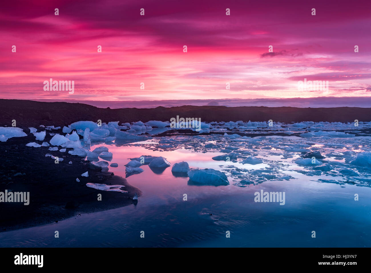 Les icebergs Jokulsarlon glacial lagoon lors d'un rouge vibrant sunrise repose immobile comme il est entouré par l'eau de mer froide. Banque D'Images