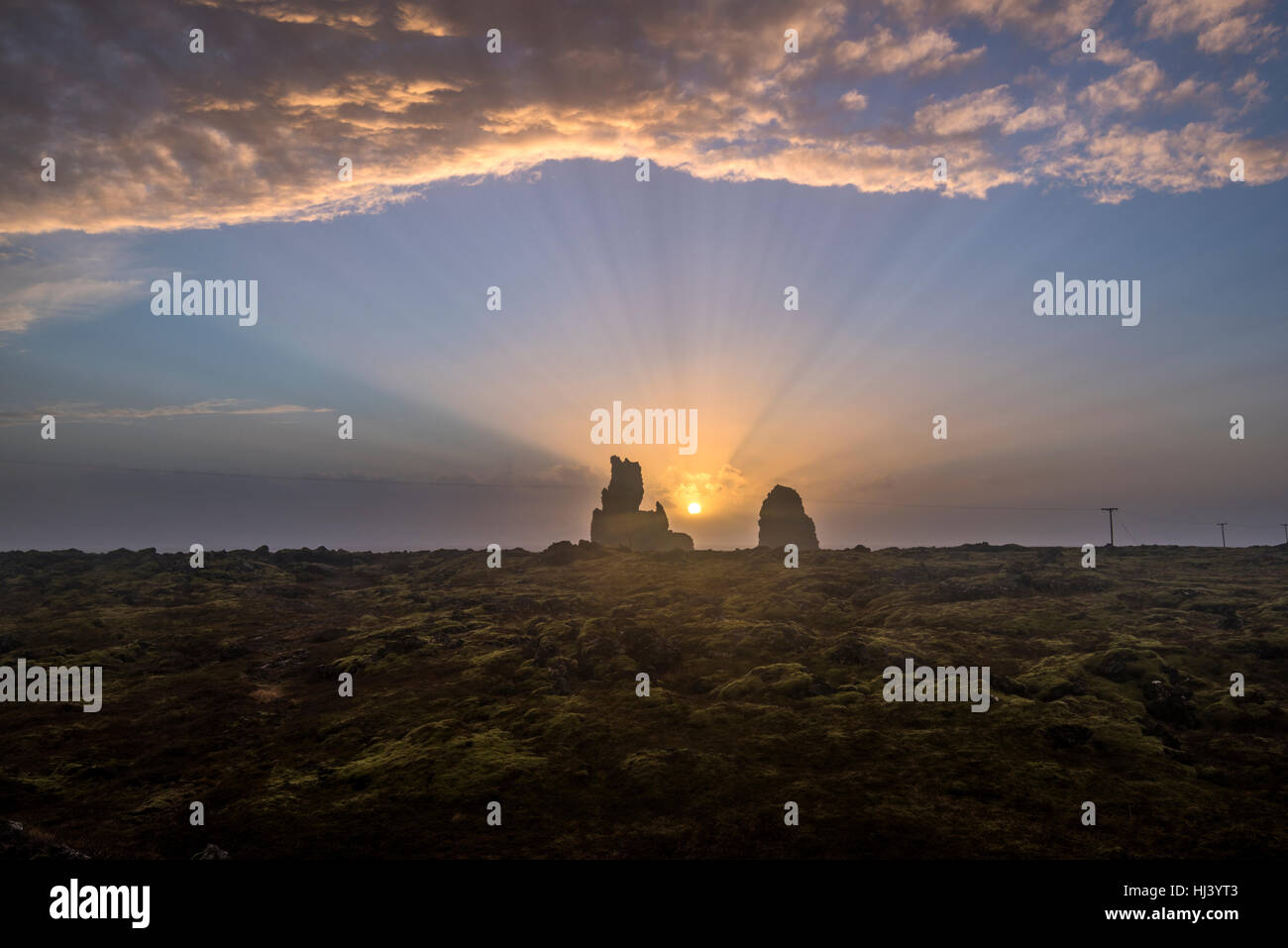 Coucher de soleil sur un paysage de l'océan montre très moody, terrain sombre encadré par un grand récif en saillie et les rayons du soleil orange casting les rayons lumineux. Banque D'Images