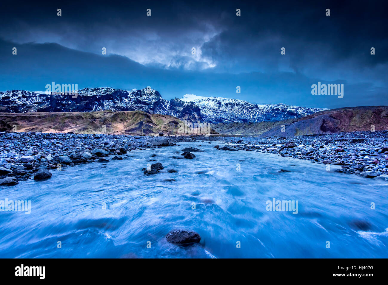 Une rivière formée par la fonte des glaciers s'écoule à travers une chaîne de montagnes dans le nord de l'Islande au cours d'une sombre, jour de pluie. Banque D'Images