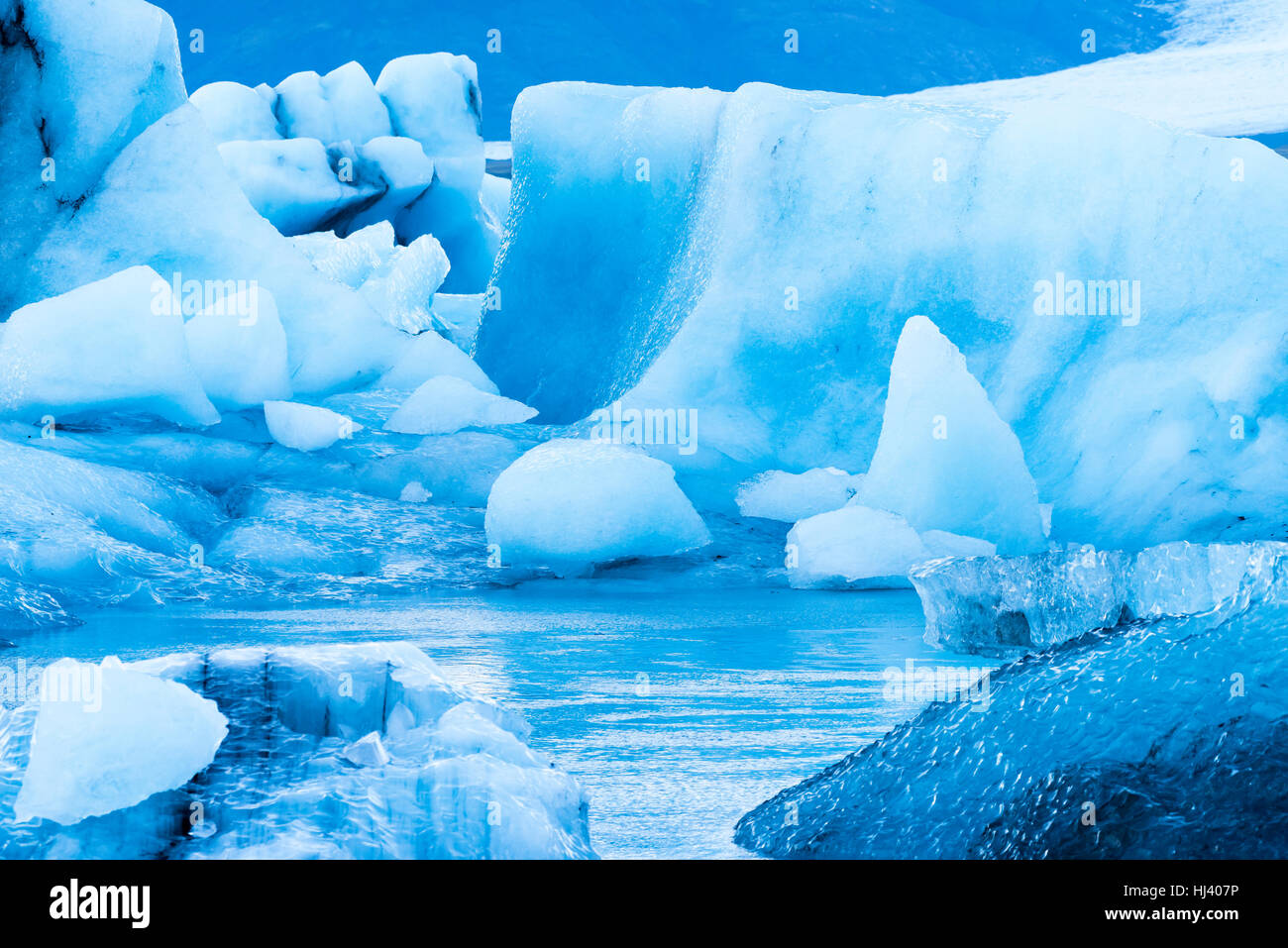 Les icebergs le long de la rive du Jokulsarlon glacial lagoon pendant un temps couvert bleu reste immobile tandis qu'encadrée par l'eau de mer froide. Banque D'Images