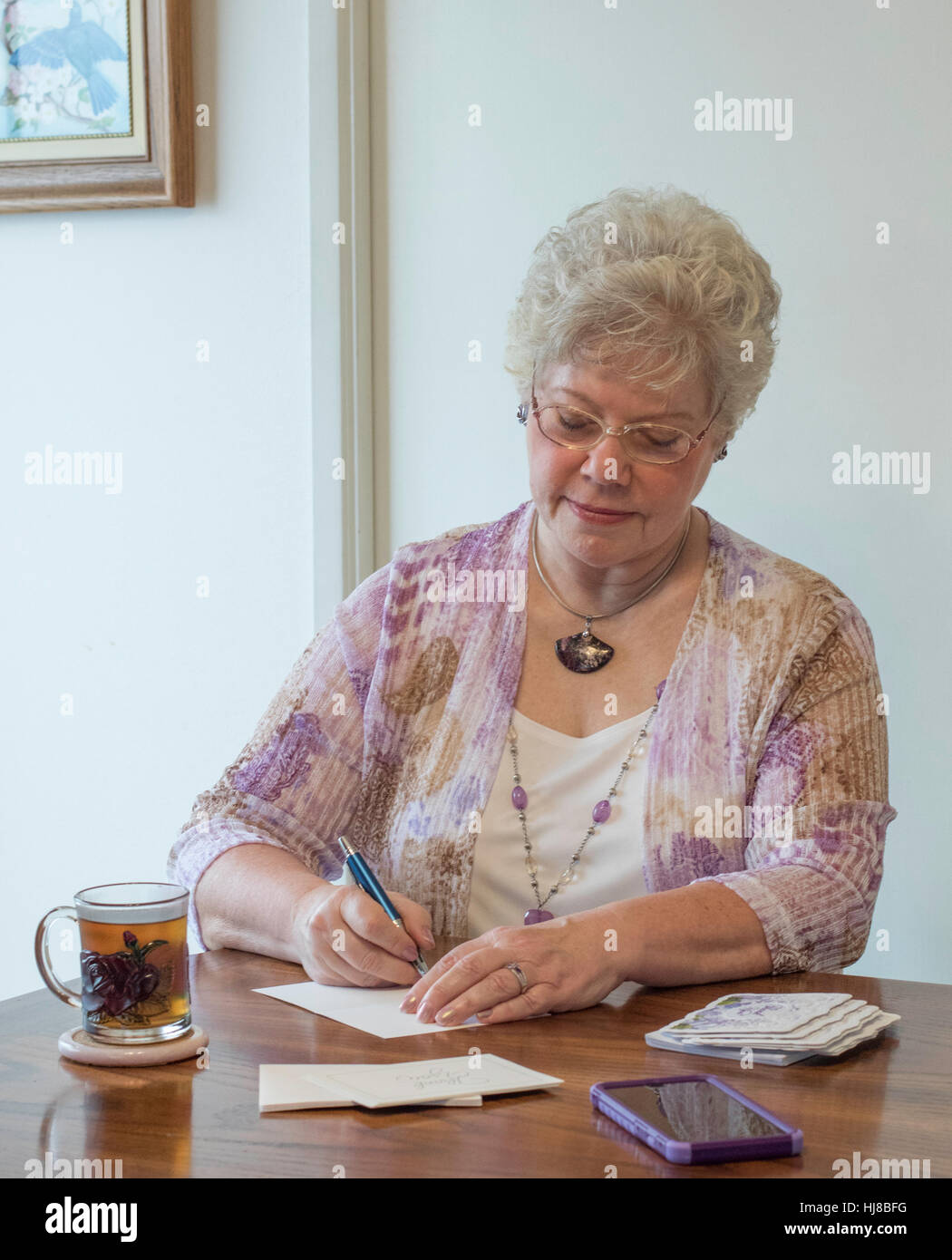 Dans une lettre d'écriture femme 70's avec un stylo et du papier et le verre clair tasse de thé. Elle est à la recherche vers le bas et se concentrer sur la tâche à accomplir. Banque D'Images