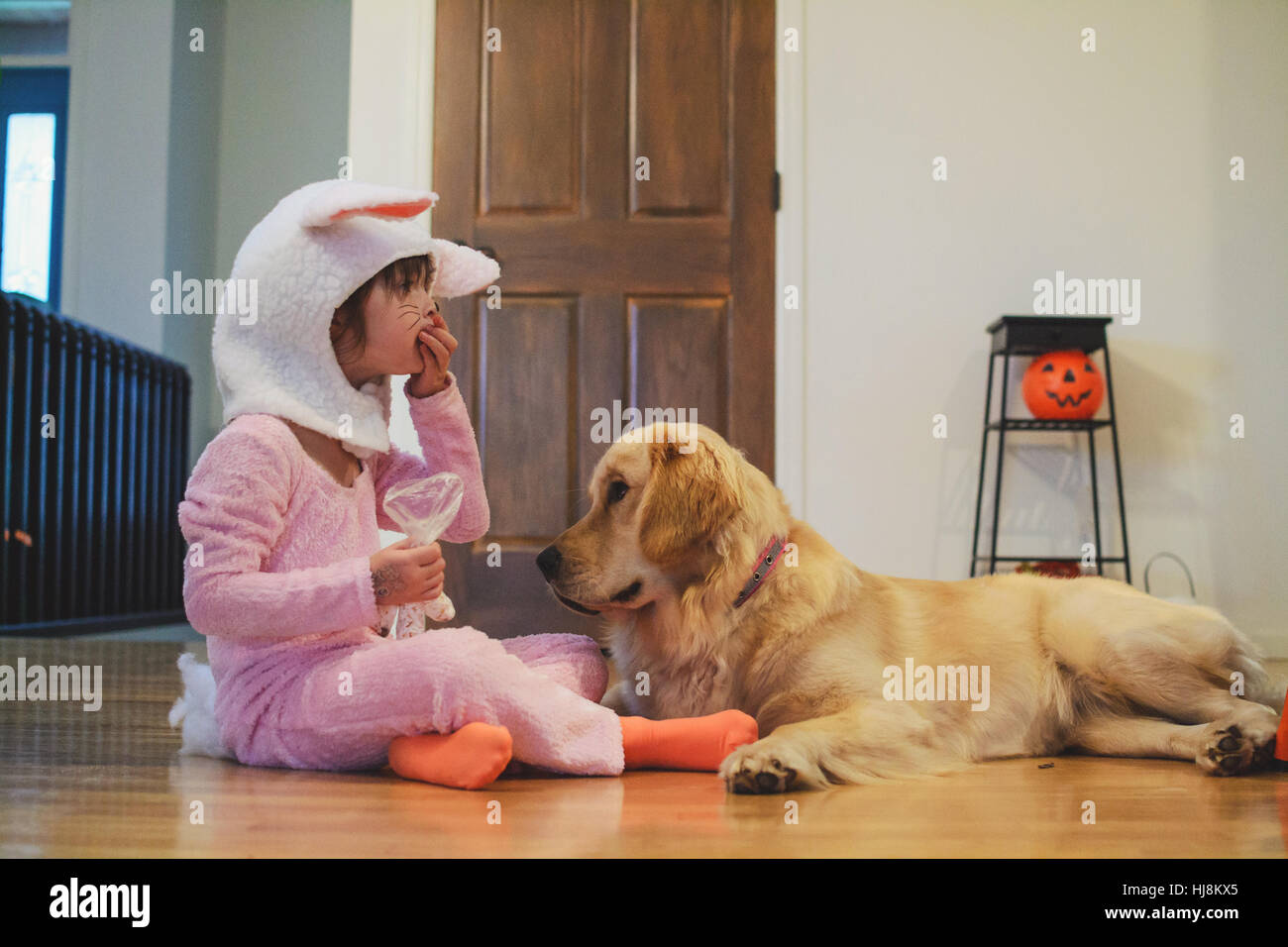 Fille en costume de lapin assis sur marbre manger bonbons d'Halloween avec Golden Retriever dog Banque D'Images