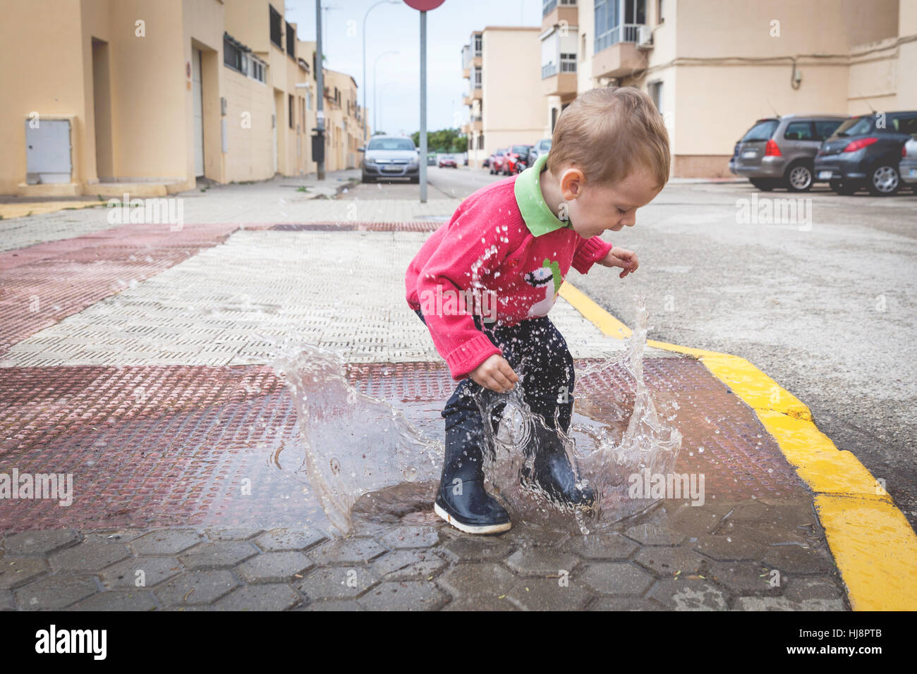 Garçon sautant dans une flaque d'eau dans la rue Banque D'Images