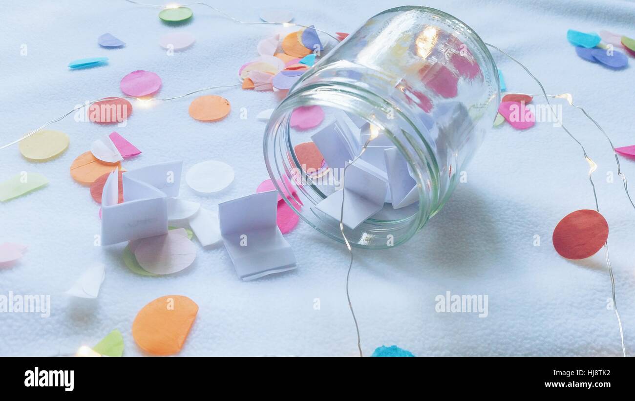 Tiens en verre bocal rempli de papier tient sur une table avec confetti Banque D'Images