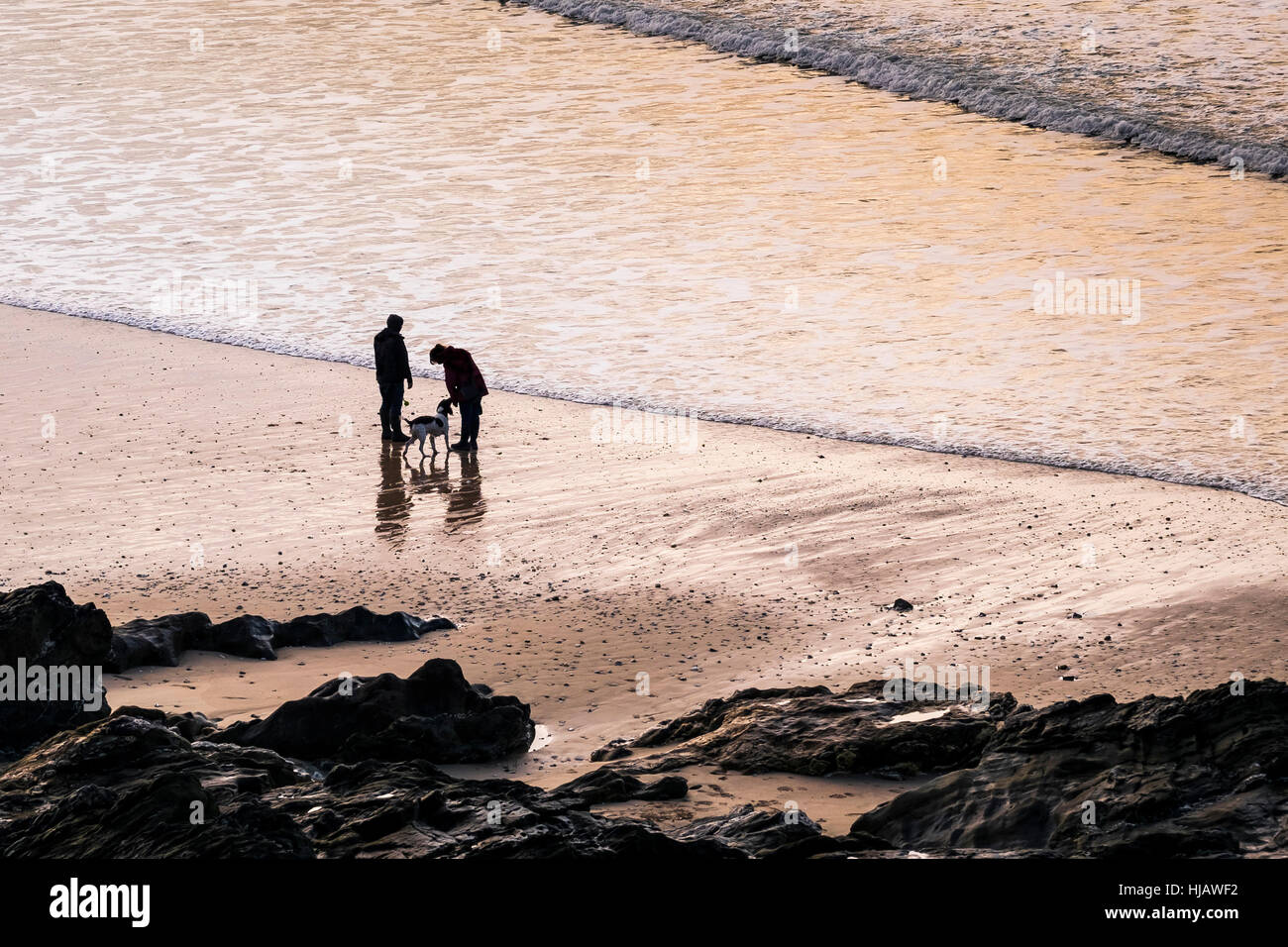 Deux personnes et leur chien vu en silhouette alors que le soleil se couche sur la plage de Fistral, Newquay, Cornwall. Banque D'Images