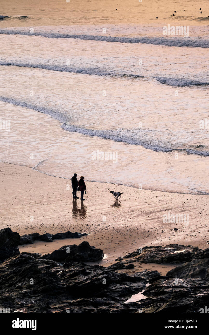 Deux personnes et leur chien vu en silhouette alors que le soleil se couche sur la plage de Fistral, Newquay, Cornwall. Banque D'Images