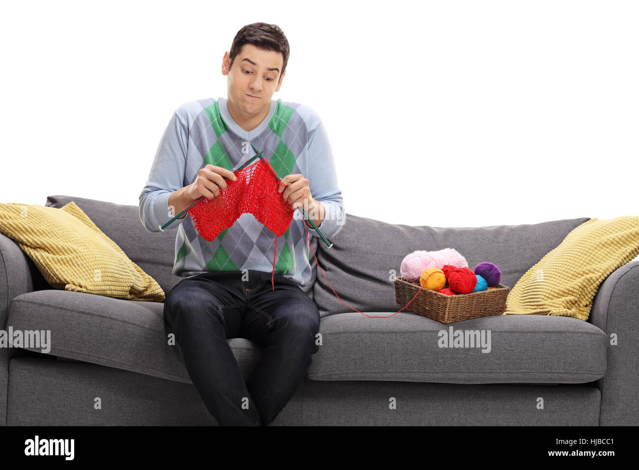 Guy confus assis sur un canapé et essayer de tricoter isolé sur fond blanc Banque D'Images
