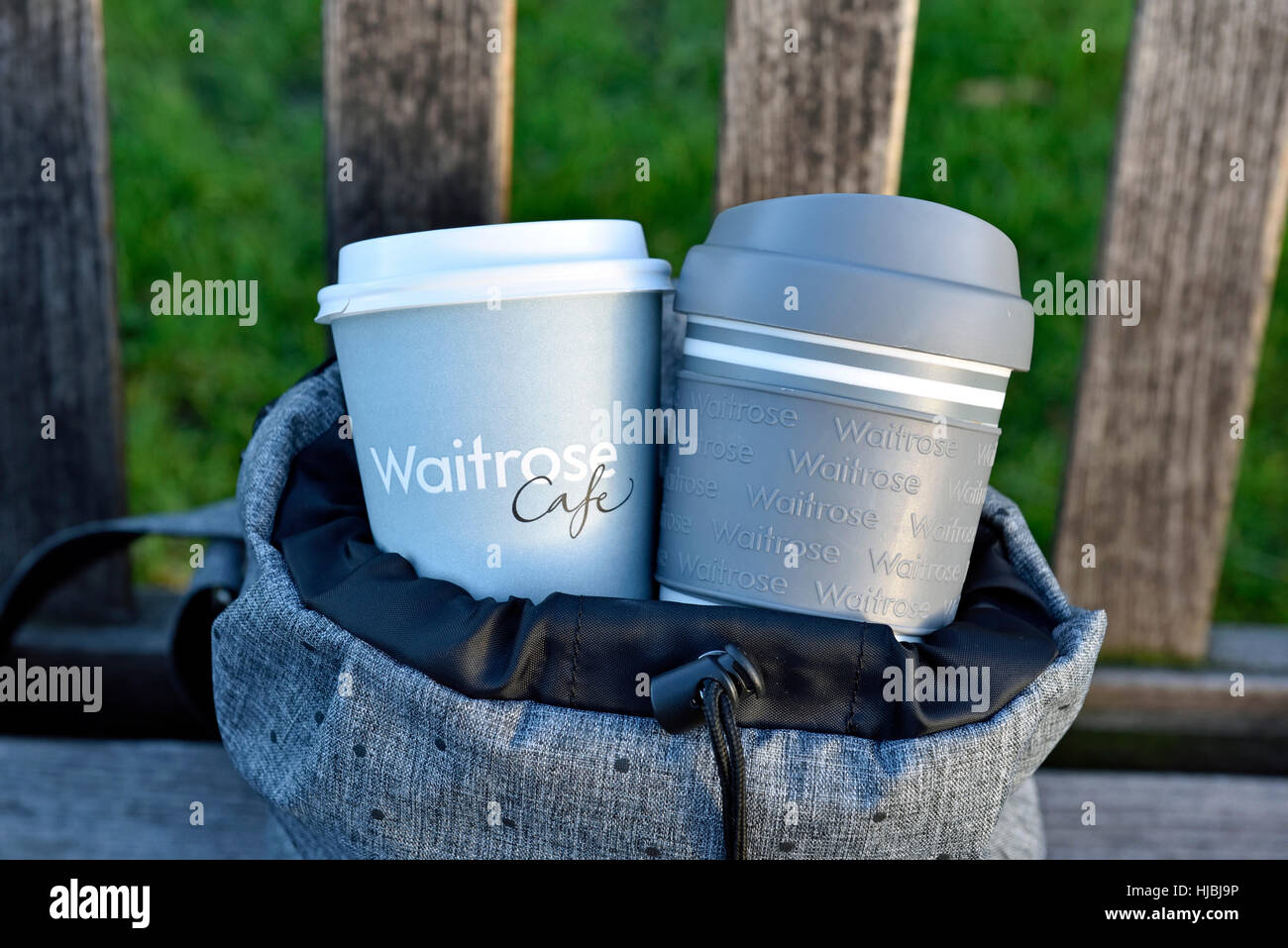 Waitrose emporter jetables et réutilisables tasse à café et tasse de voyage en sac à dos gris urbain intelligent sur banc de parc, le centre de Londres Banque D'Images
