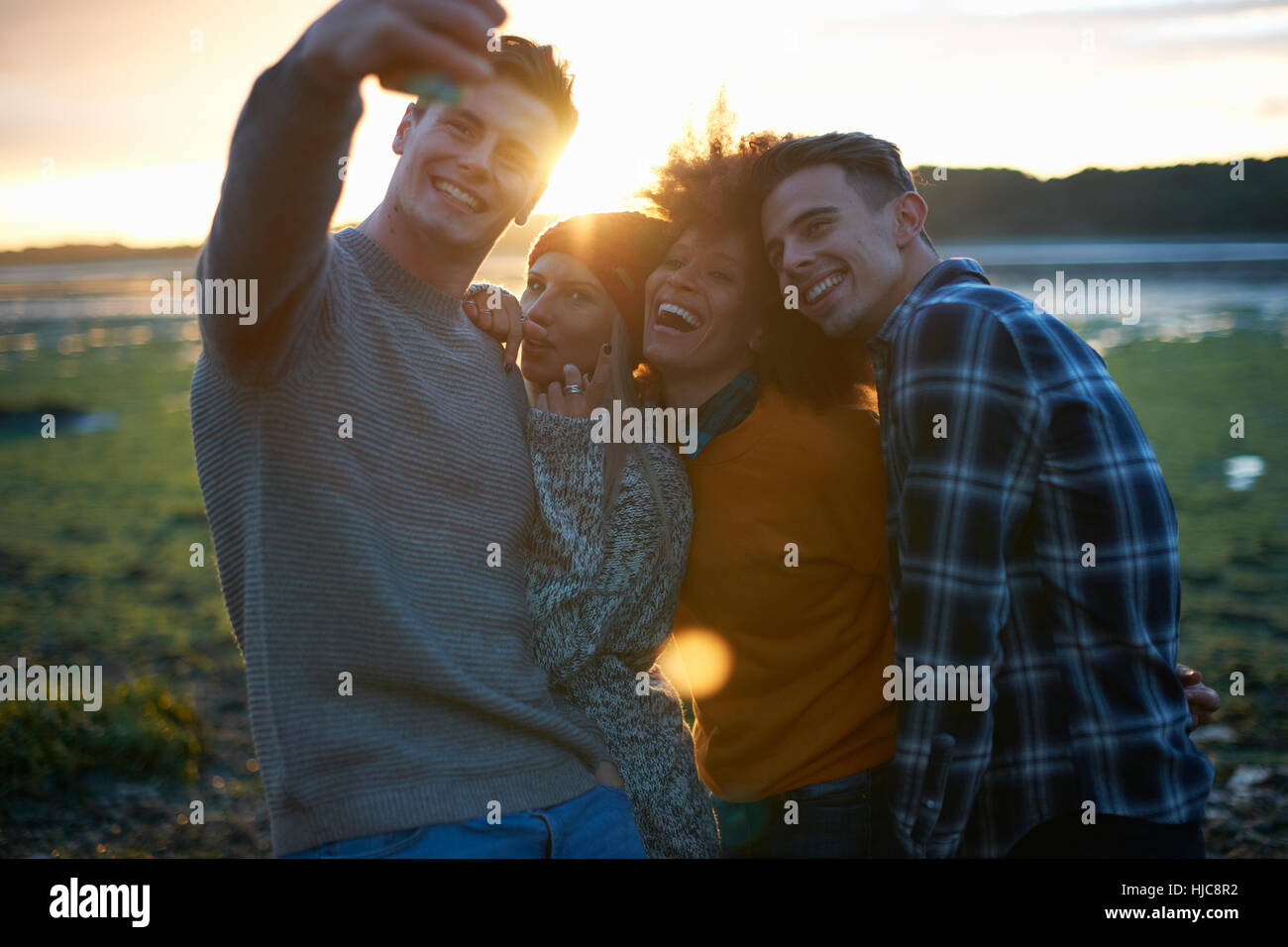 Quatre jeunes adultes qui suivent le coucher du soleil à seaside selfies smartphone Banque D'Images