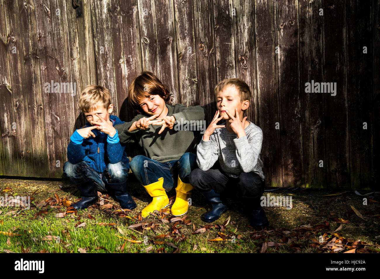 Trois garçons, à l'extérieur, accroupi à côté de clôture, faire les gestes de la main Banque D'Images