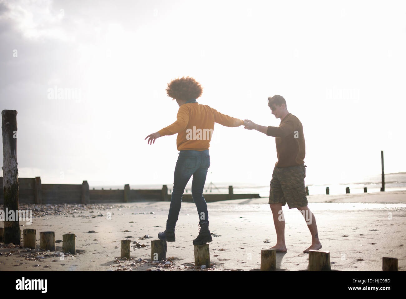 Man helping woman équilibre sur les souches en bois on beach Banque D'Images