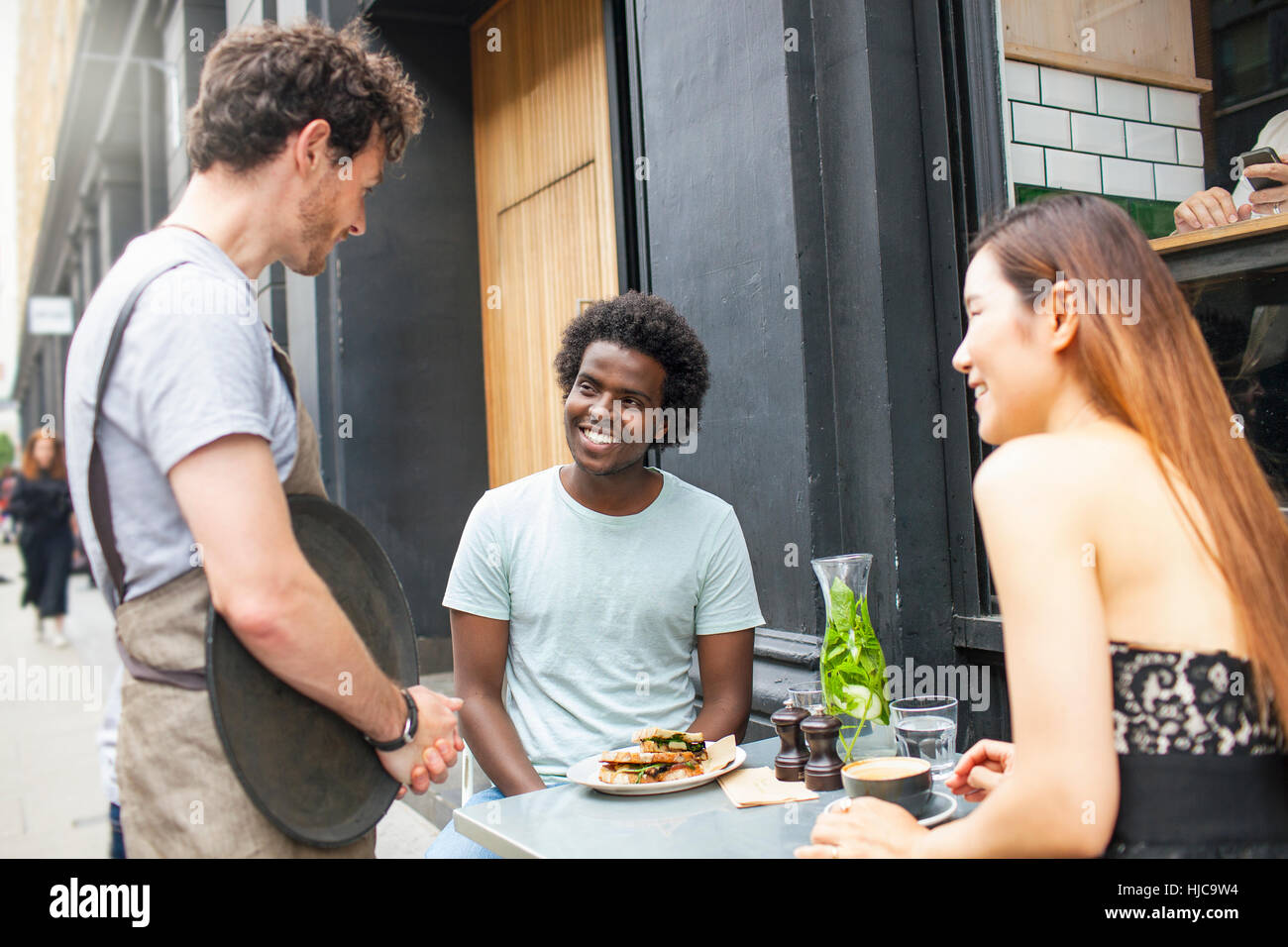 Waiter serving couple at city sidewalk cafe Banque D'Images