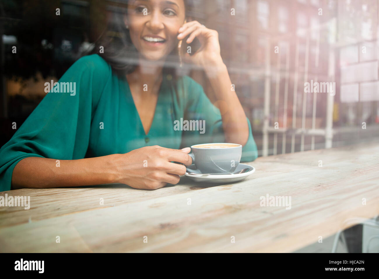 Mid adult woman chatting on smartphone in cafe siège de fenêtre Banque D'Images