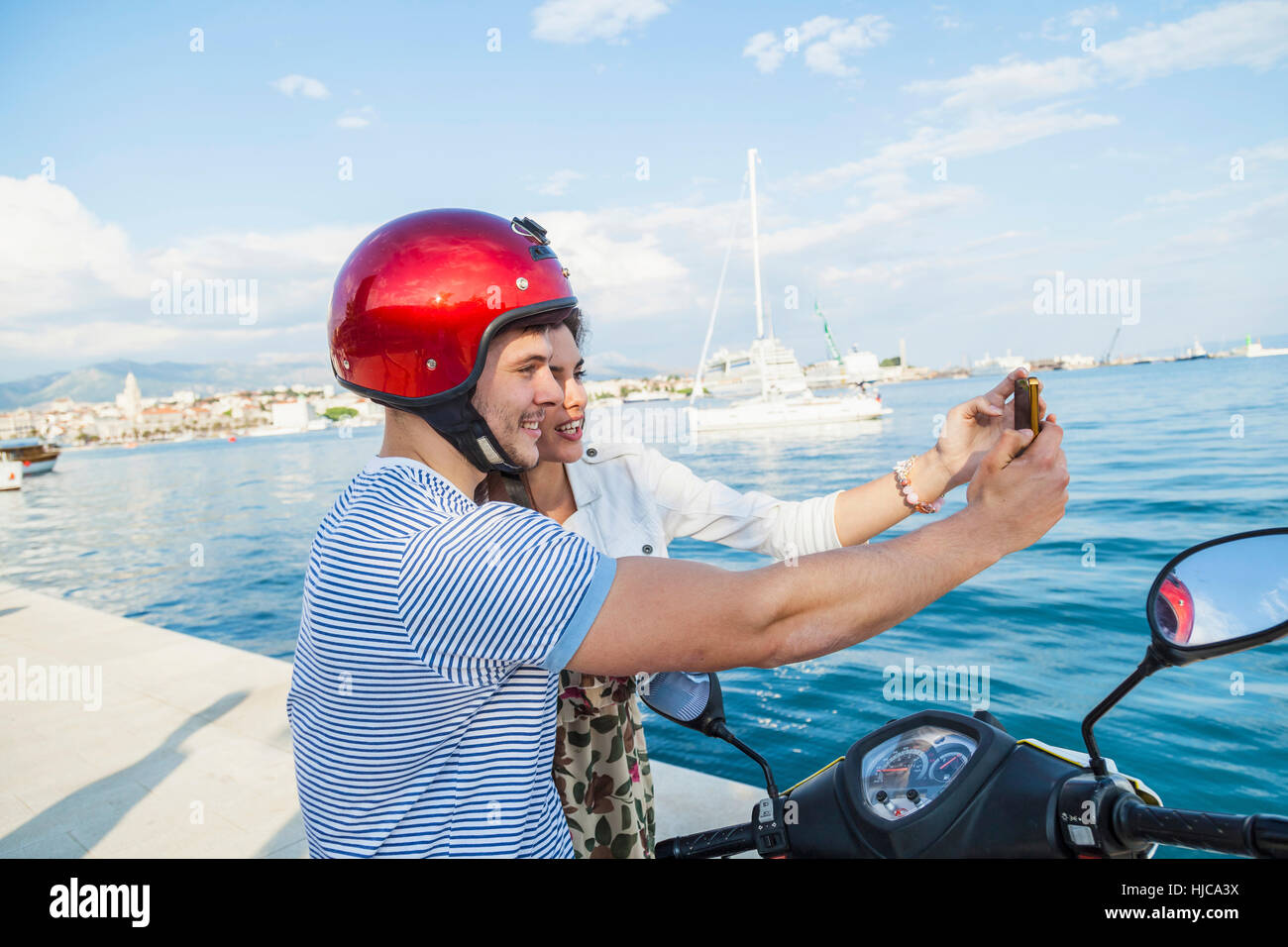 Jeune couple de cyclomoteurs en tenant à l'Harbour selfies, Split, Dalmatie, Croatie Banque D'Images