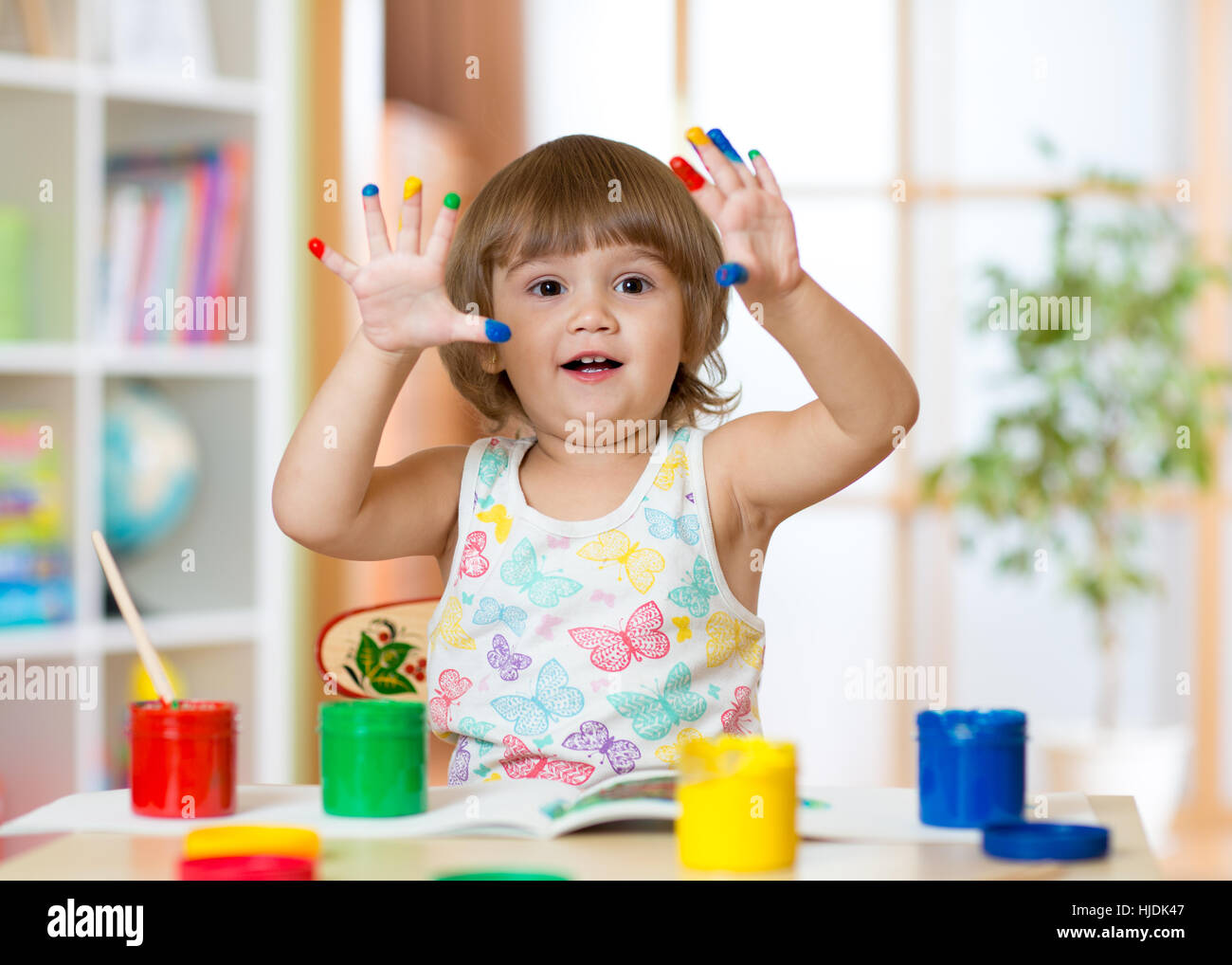 Cute cheerful kid girl montrant ses doigts peints dans des couleurs vives Banque D'Images