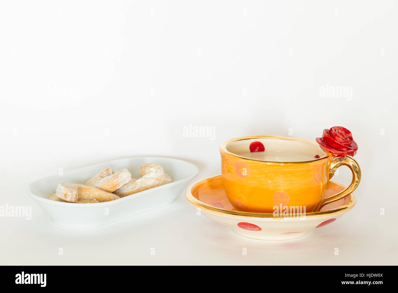 Un bel orange fait main golden cup avec ornement rose rouge, de lait et de délicieux biscuits sur une plaque blanche Banque D'Images