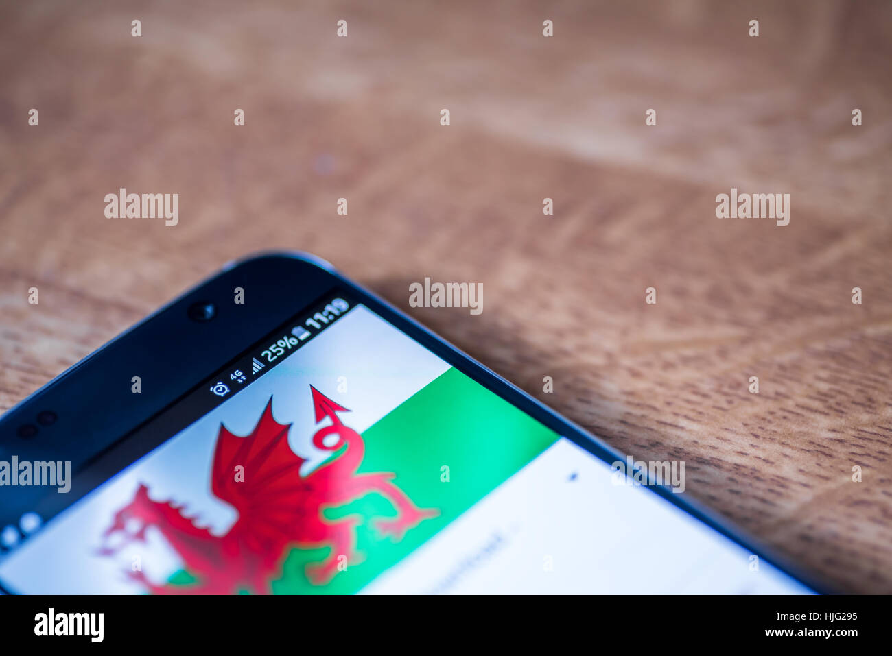 Smartphone sur fond de bois avec 4G Réseau inscription 25  % et le Pays de Galles drapeau sur l'écran. Banque D'Images