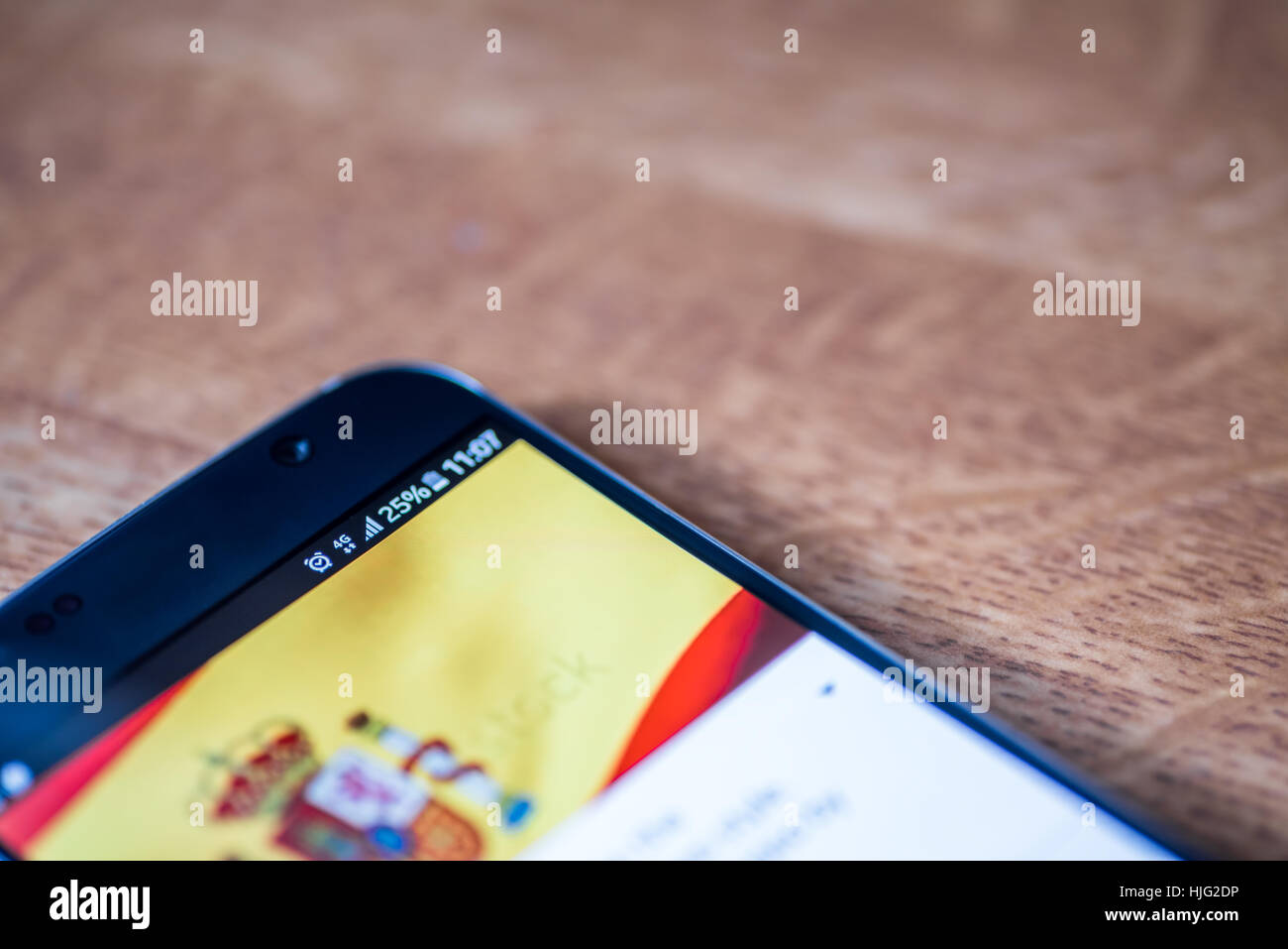 Smartphone sur fond de bois avec 4G Réseau inscription 25  % et l'Espagne drapeau sur l'écran. Banque D'Images
