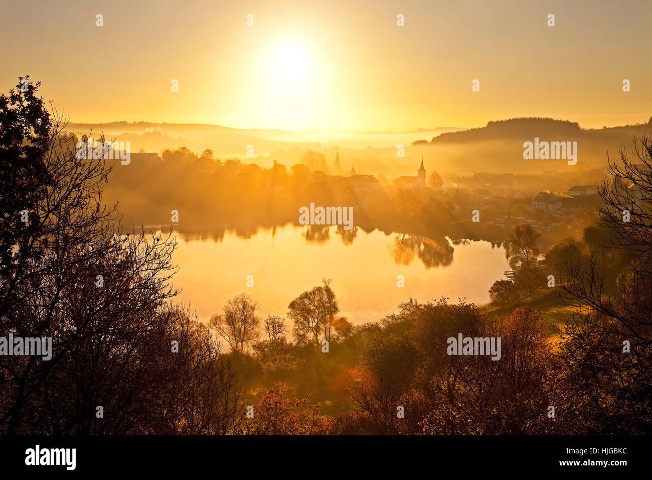 Ville avec l'église, près du lac Schalkenmehrener Maar, à l'automne au lever du soleil, de l'eau reflet, Schalkenmehren, Daun Vulkaneifel, Banque D'Images