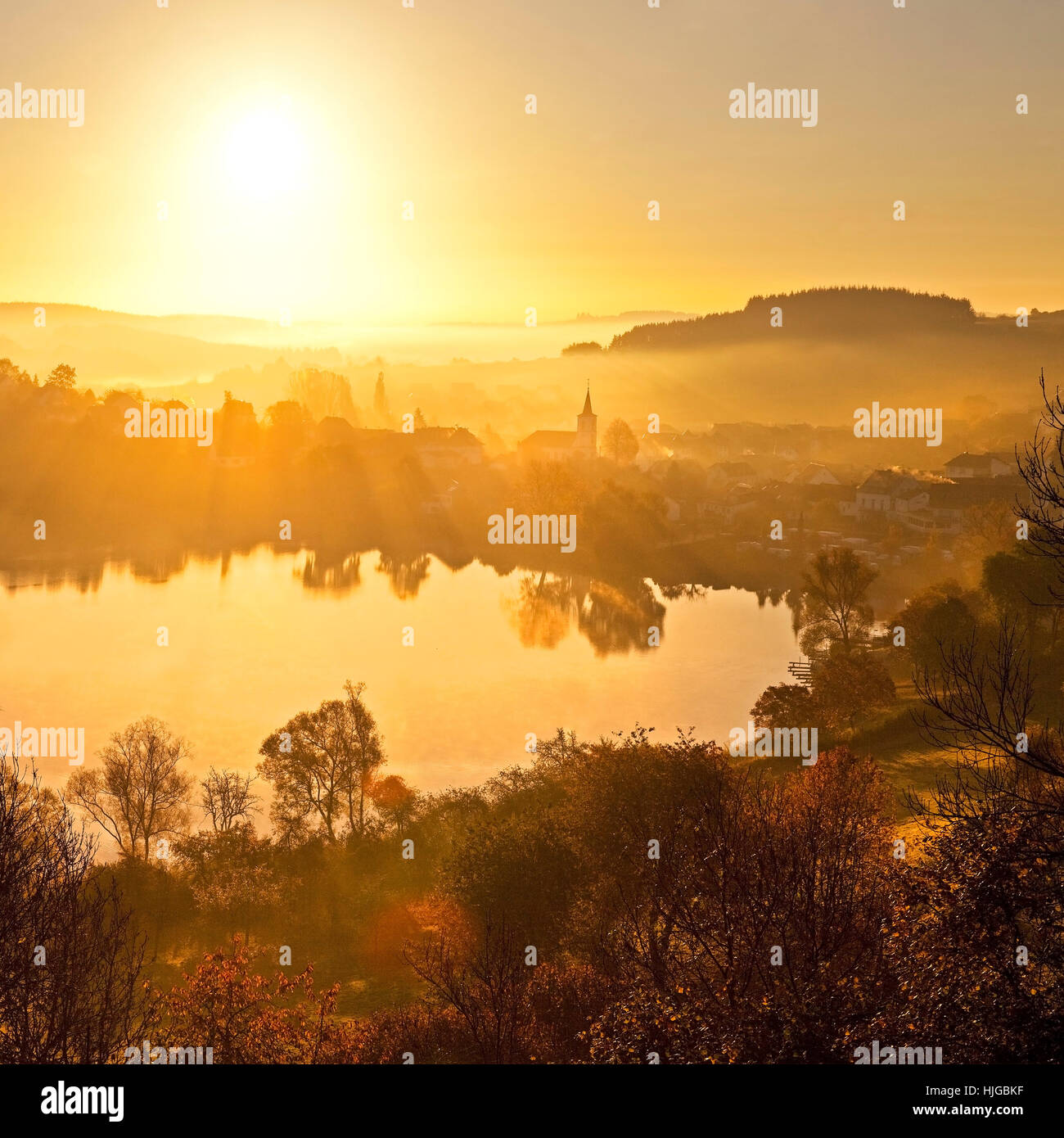 Ville avec l'église, près du lac Schalkenmehrener Maar, à l'automne au lever du soleil, de l'eau reflet, Schalkenmehren, Daun Vulkaneifel, Banque D'Images