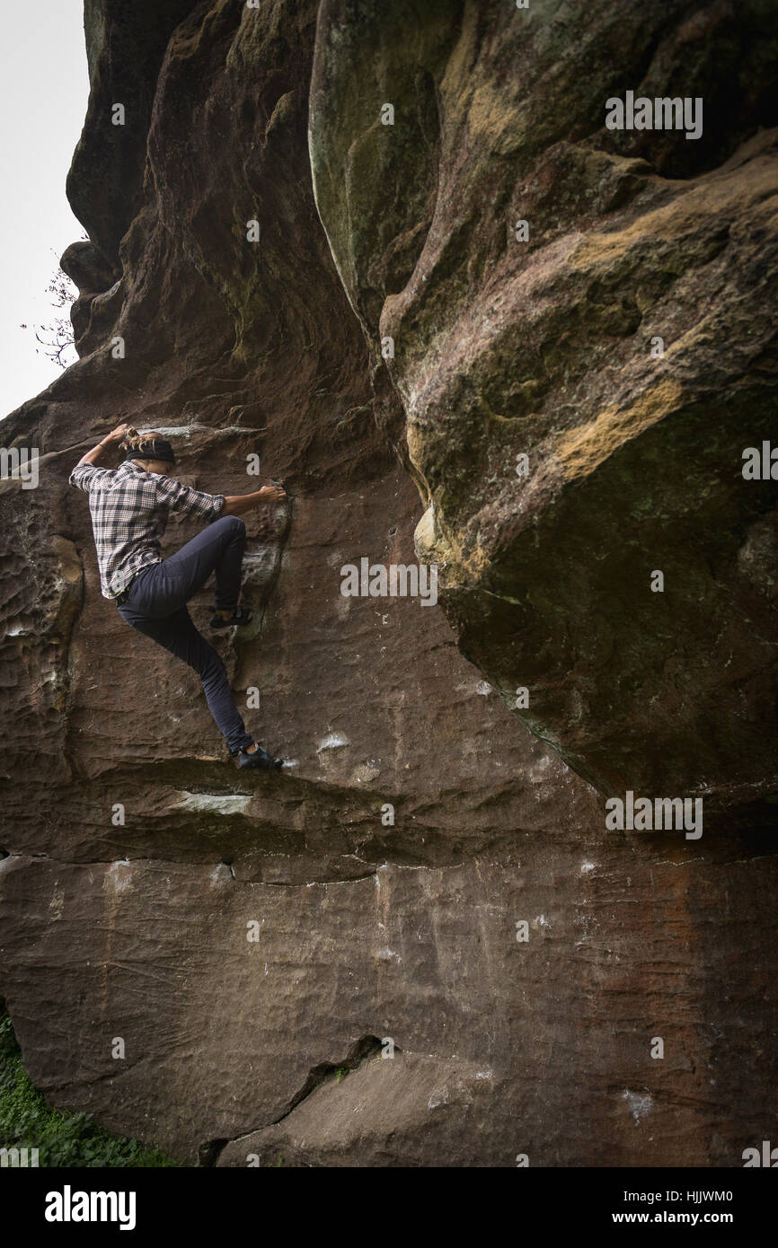 Un female rock climber climbing a boulder sans cordes, portant des jeans et une chemise. Banque D'Images