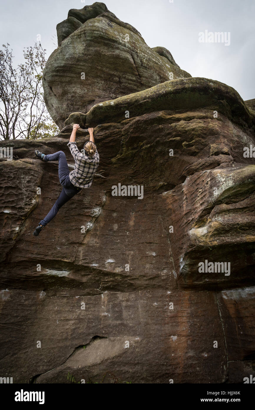 Un female rock climber climbing a boulder sans cordes, portant des jeans et une chemise. Banque D'Images