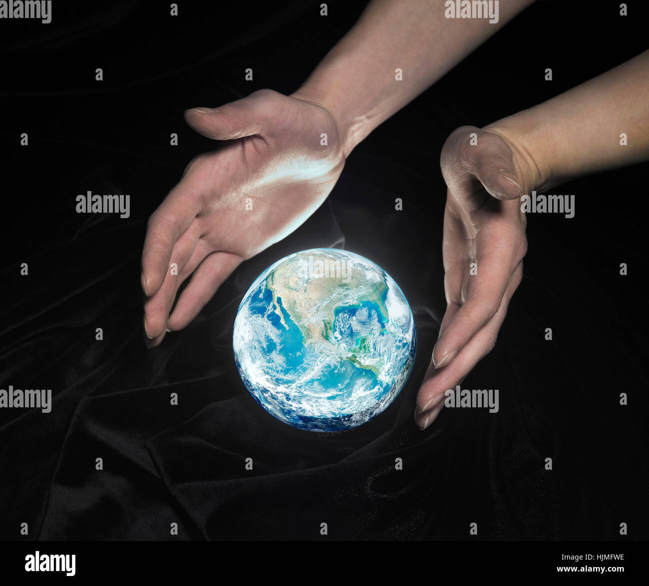 High angle shot d'un globe de cristal brillant entouré de tissus crinkly noir et deux mains autour de Banque D'Images