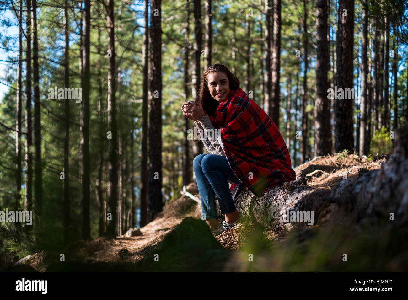 Souriante jeune femme avec couverture et de boissons dans la forêt Banque D'Images