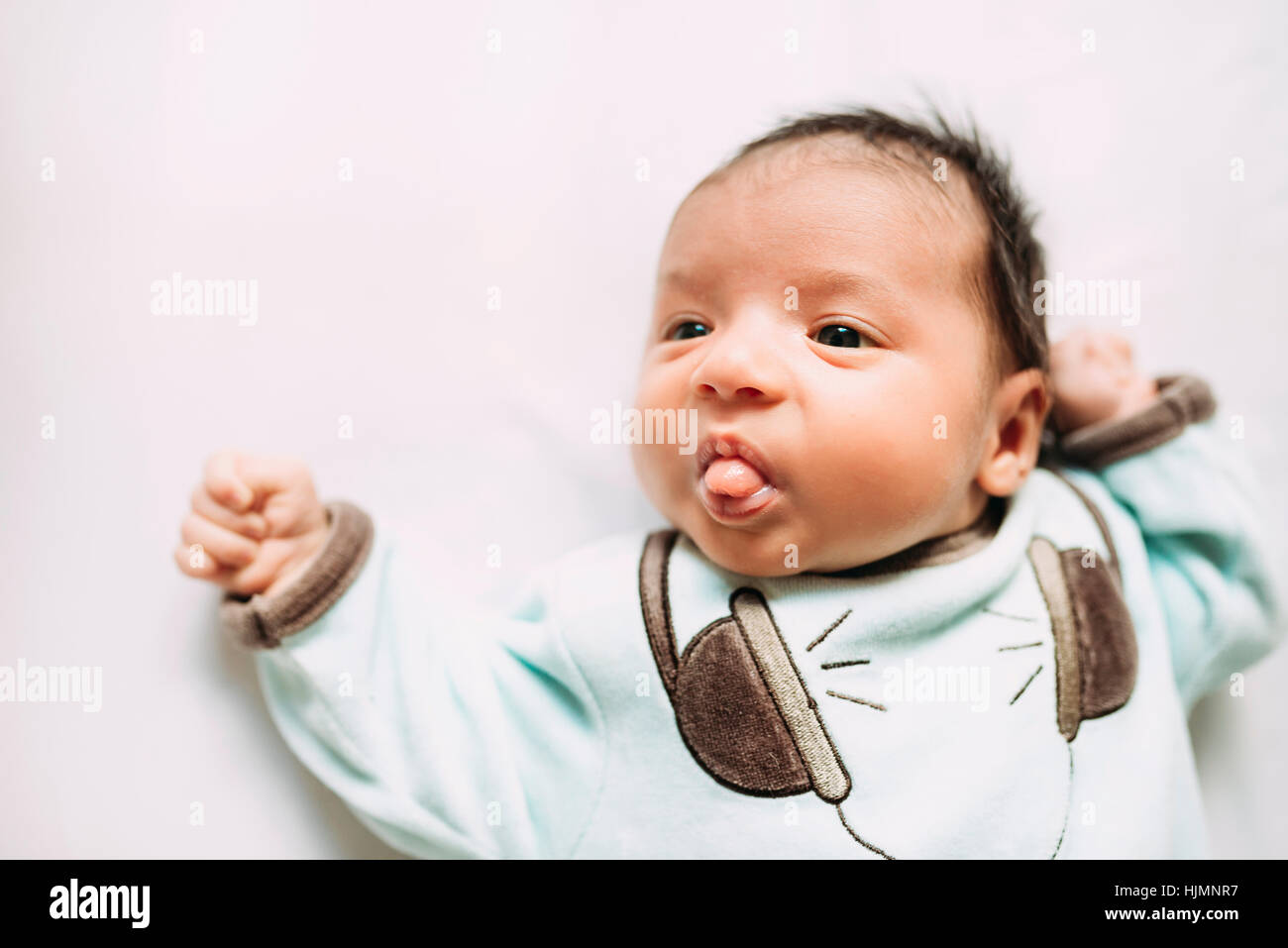 Newborn baby girl lying on bed sticking out tongue Banque D'Images