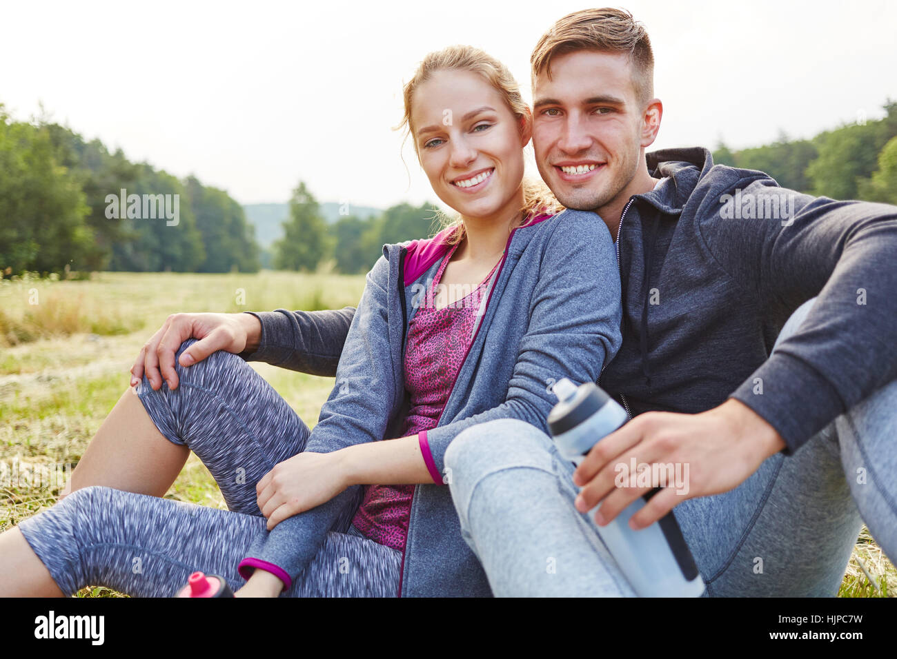 Couple amoureux heureux assis sur l'herbe pendant un voyage de randonnée Banque D'Images