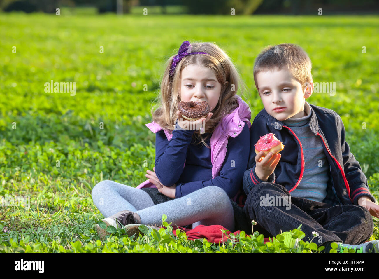 Happy kids eating donuts assis sur l'herbe verte dans le parc Banque D'Images