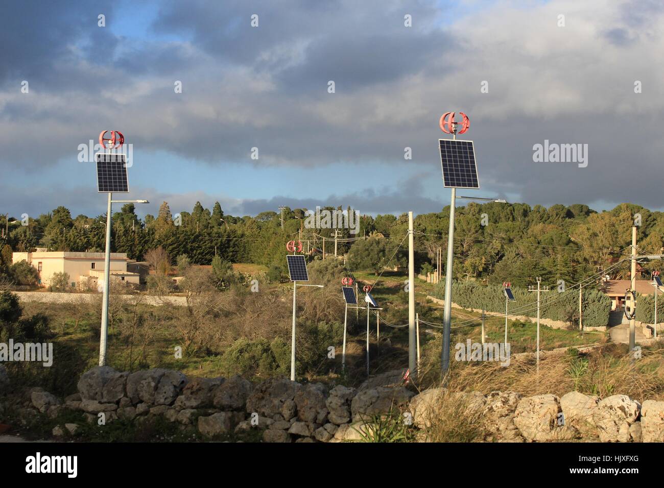 Sur une ruelle rural en Sicile, l'éclairage de rue alimenté par des panneaux solaires et éoliennes ponctuent le paysage sous un ciel d'orage. Banque D'Images