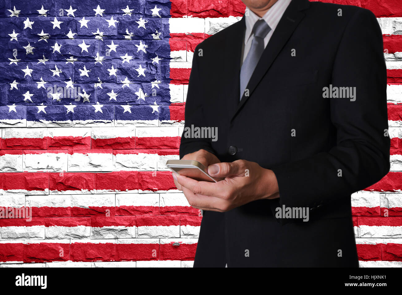 L'homme d'affaires de l'écran tactile du téléphone intelligent à la main et des murs de brique peints en United States flag (USA) comme la communication avec puissante nation concept. Banque D'Images