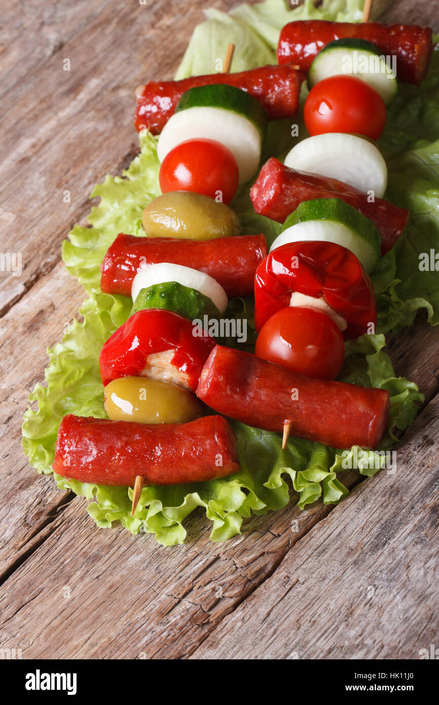 Petites saucisses grillées avec des légumes sur les brochettes sur une vieille table libre à la verticale. Banque D'Images