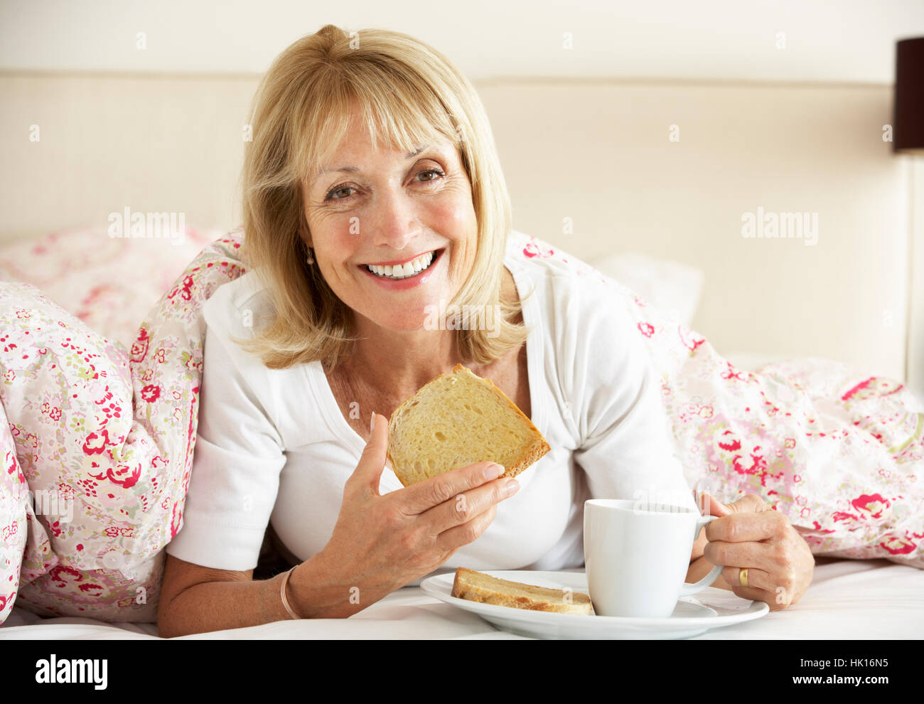 Senior Woman se blottit sous couette Eating Breakfast Banque D'Images