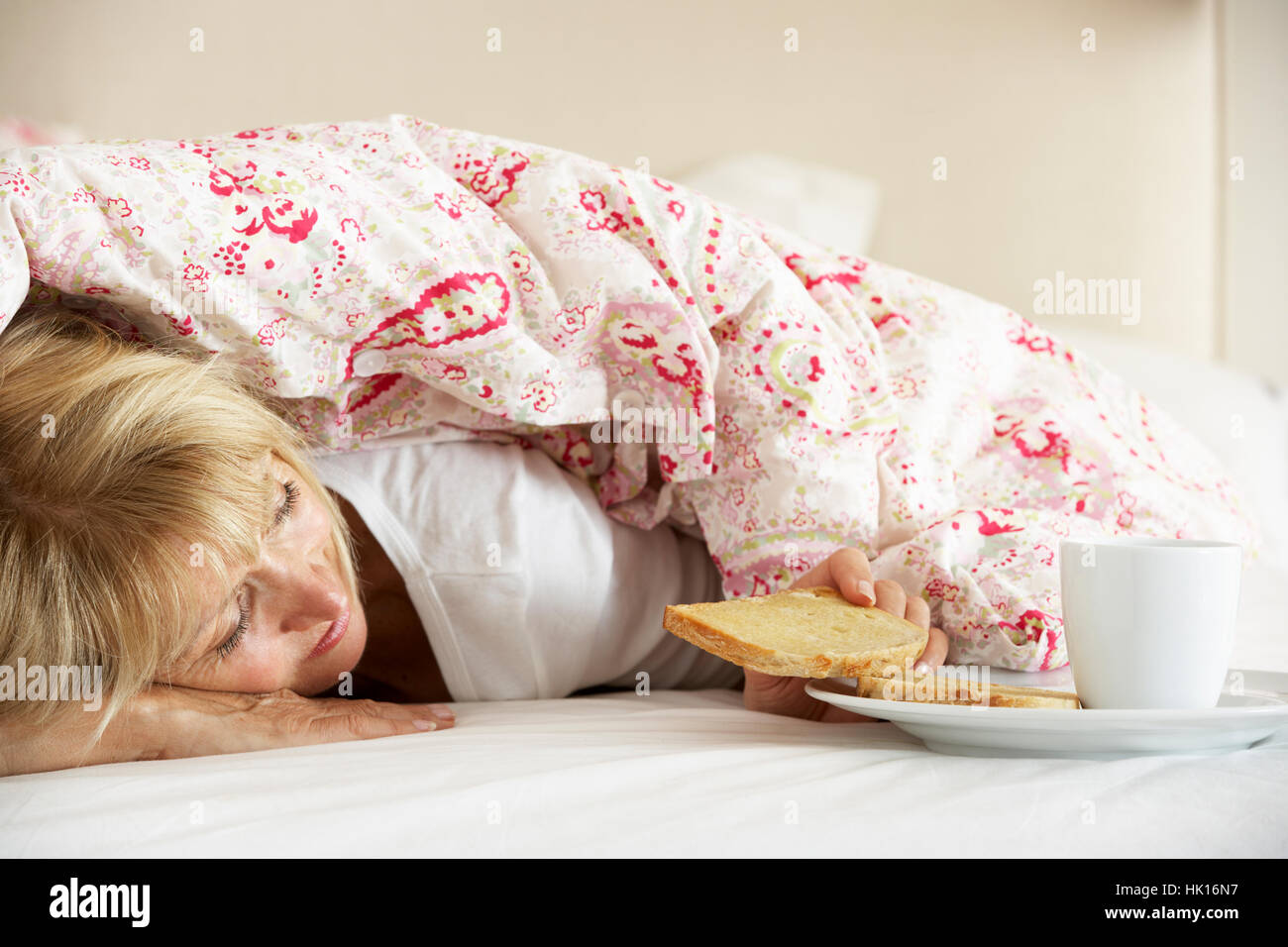 Senior Woman se blottit sous couette Eating Breakfast Banque D'Images