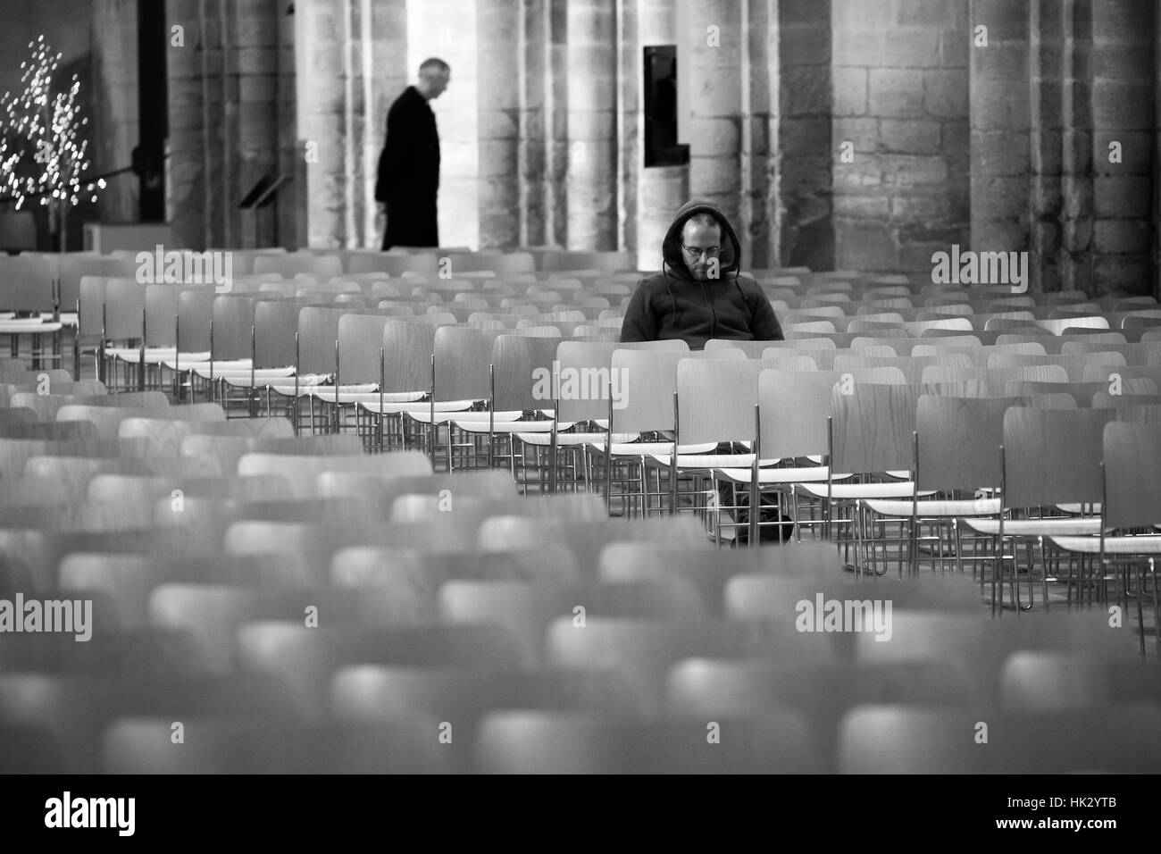 Un homme dans une contemplation profonde ou la prière dans la Cathédrale d'Ely avec un prêtre dans l'arrière-plan. Banque D'Images