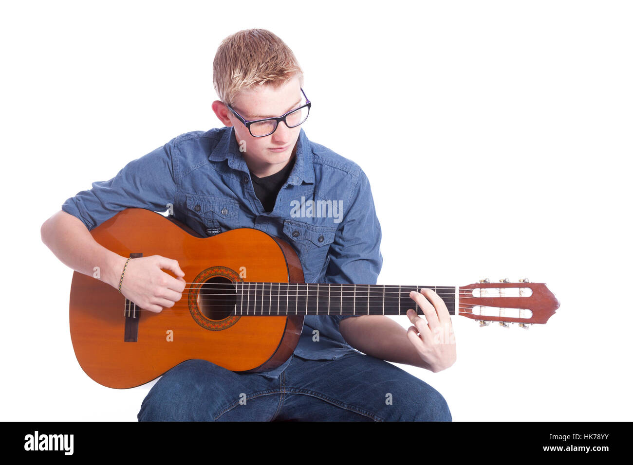 Young teen garçon en bleu porte des lunettes et joue la guitare classique en studio against white background Banque D'Images