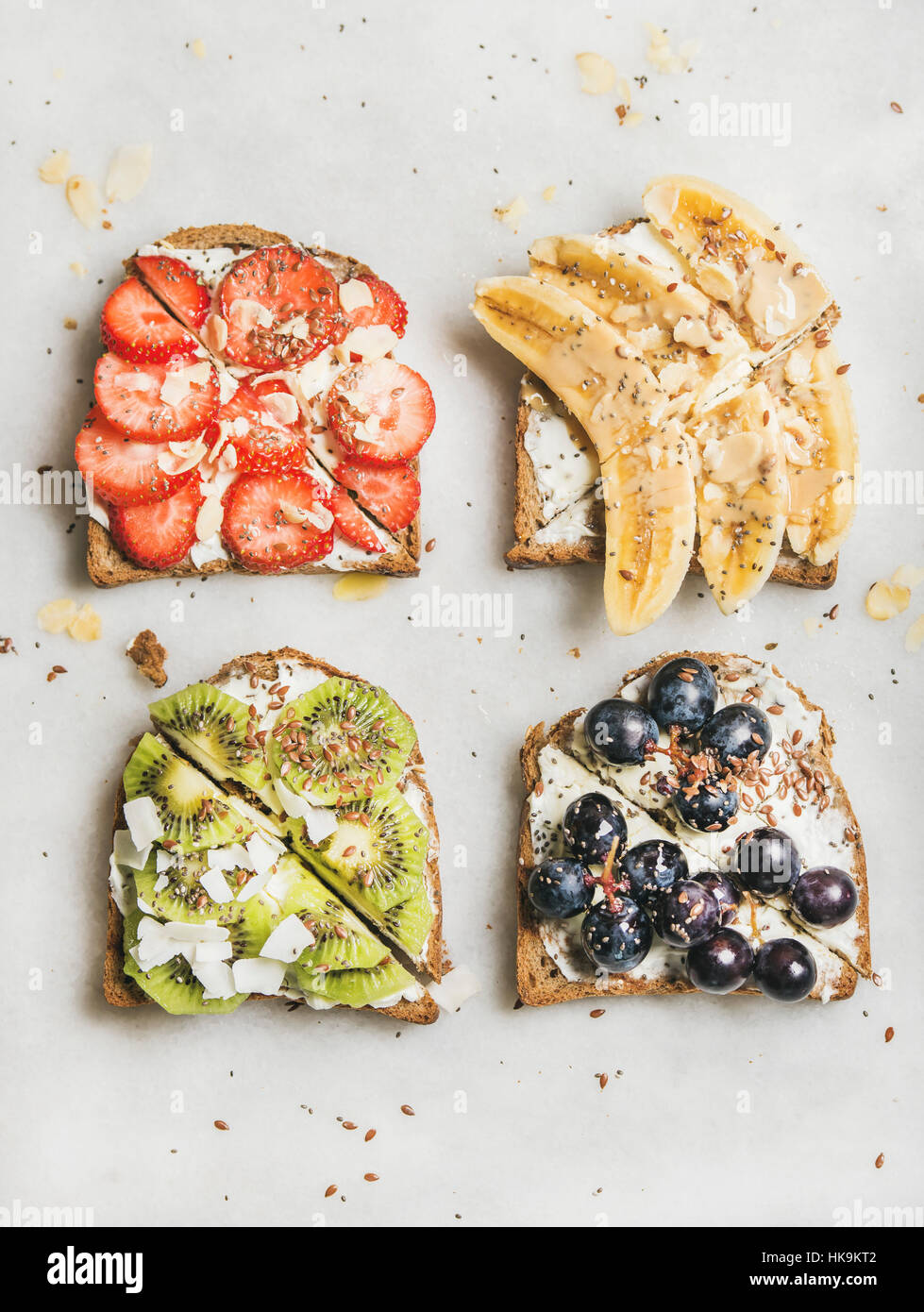 Petit-déjeuner sain des toasts. Les tranches de pain à grains entiers avec du fromage à la crème, divers fruits, graines et noix. Vue d'en haut, gris en arrière-plan Banque D'Images