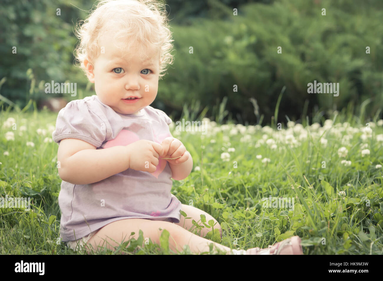 Petite fille timide sur l'herbe parmi les fleurs fleurissent en été Parc en journée ensoleillée avec copie espace Banque D'Images