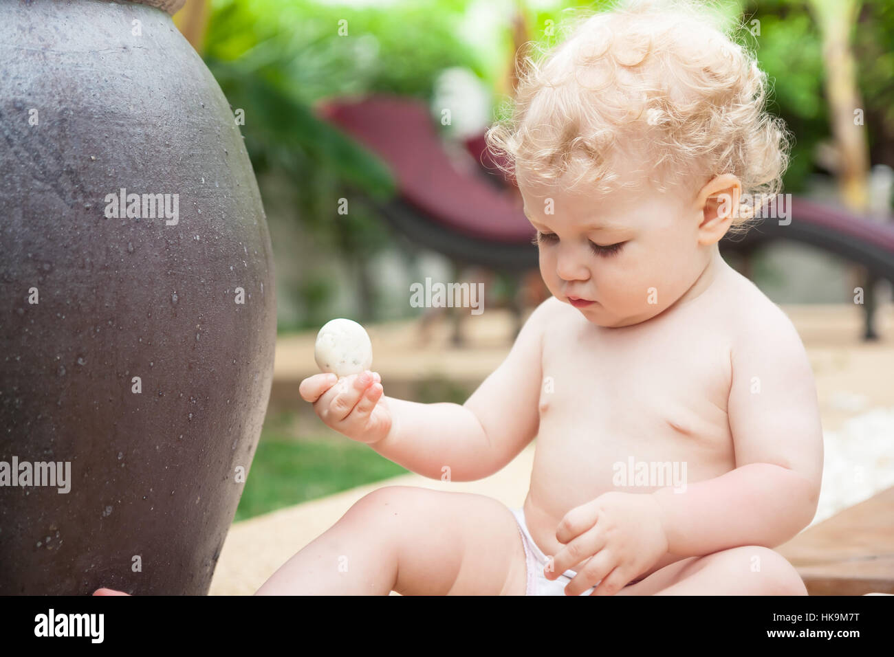 Curieux Bébé zen fille jouant avec pierre dans jardin zen tropical Banque D'Images