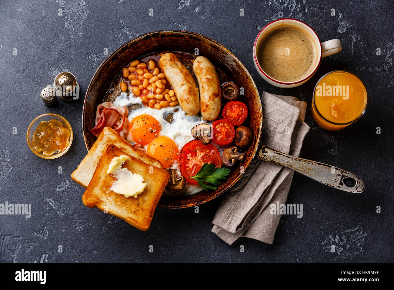 Petit-déjeuner anglais dans la casserole avec les œufs, saucisses, bacon, haricots, des toasts et du café à l'arrière-plan en pierre sombre Banque D'Images