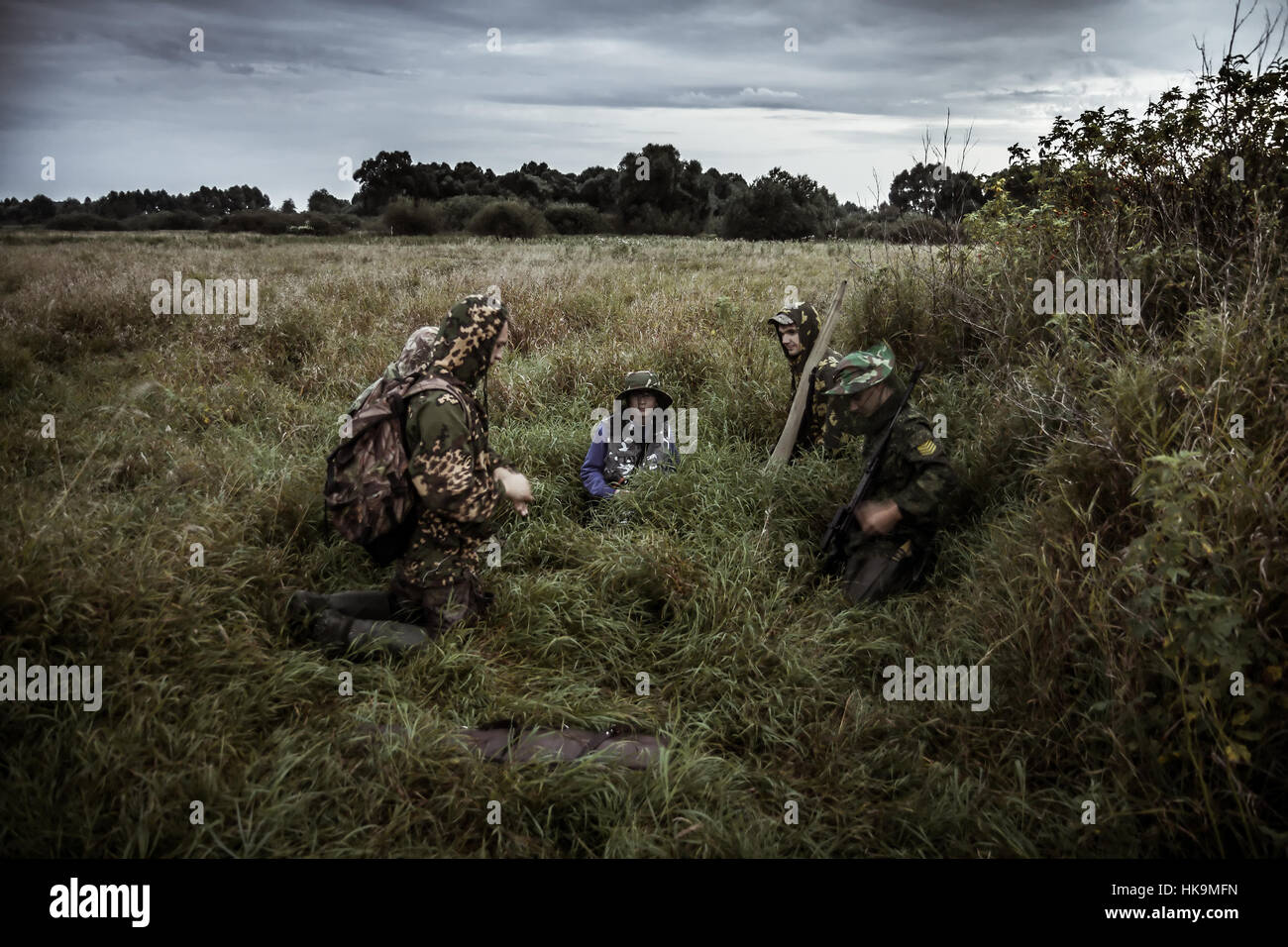 Scène de chasse avec groupe de chasseurs dans les régions rurales de champ avec ciel dramatique dans l'attente de la chasse dans les hautes herbes pendant la saison de la chasse Banque D'Images