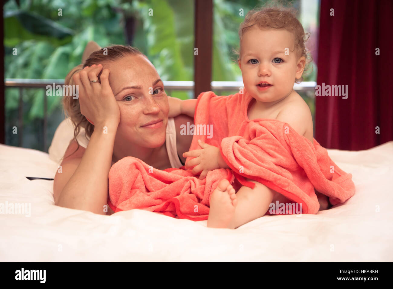 Mother with baby daughter relaxing on lit dans votre intérieur. Enfant embrassant sa mère et ils ont tous deux à la recherche de l'appareil photo. Banque D'Images