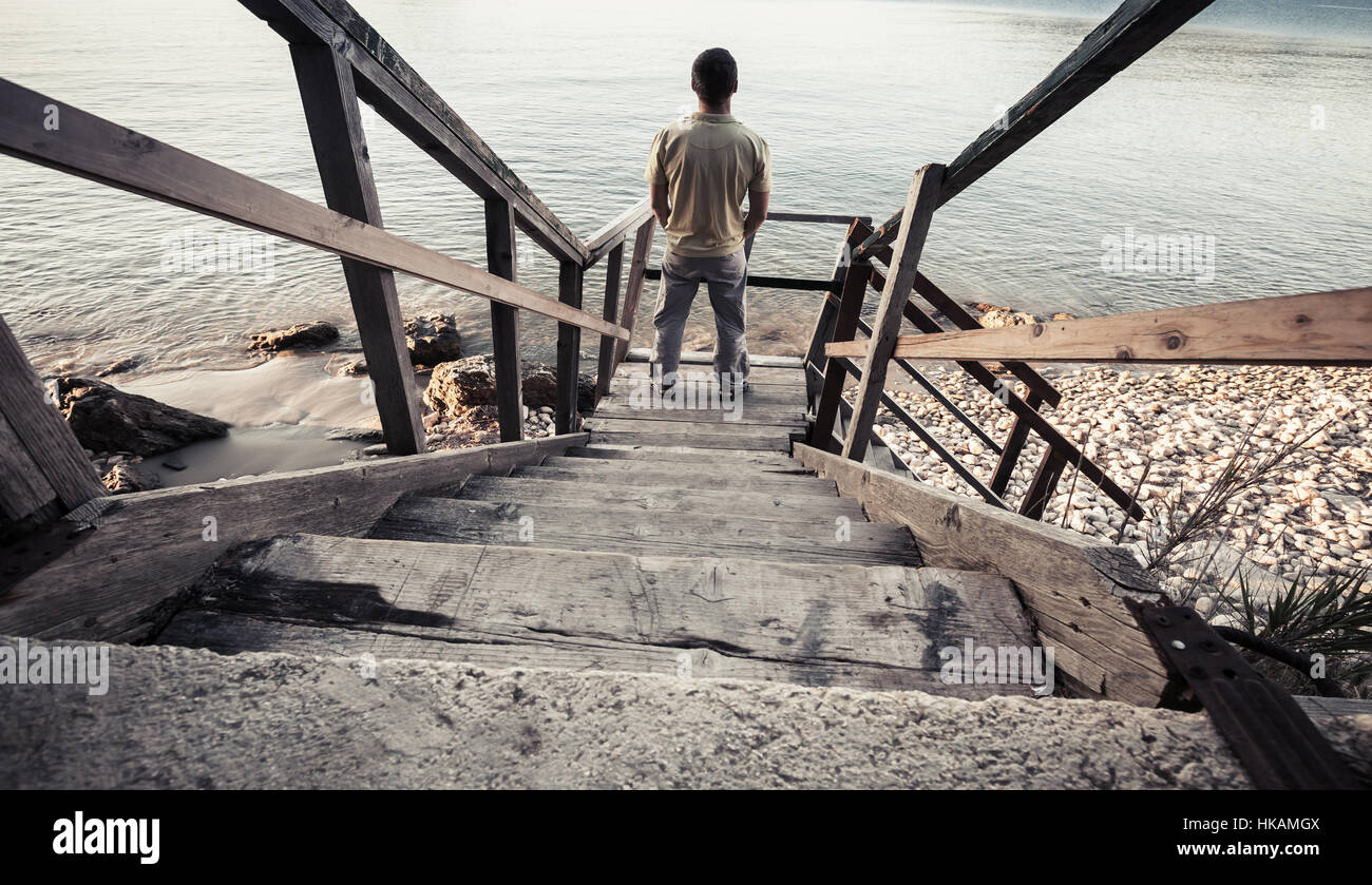 Jeune homme se dresse sur l'ancien escalier en bois qui descend jusqu'à la côte. Vintage photo aux couleurs, style ancien filtre photo Banque D'Images