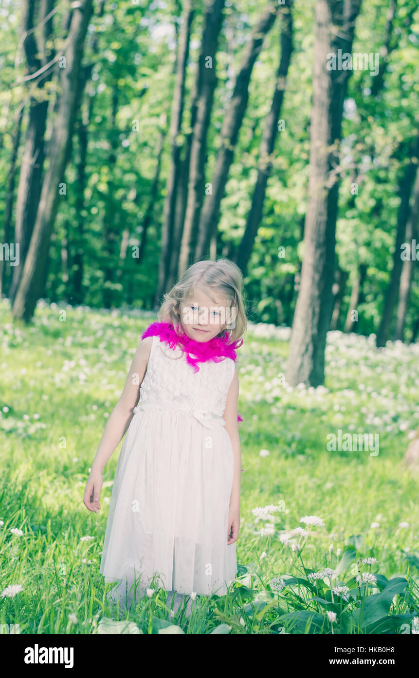 Belle petite fille blonde avec boa pourpre au printemps woods Banque D'Images