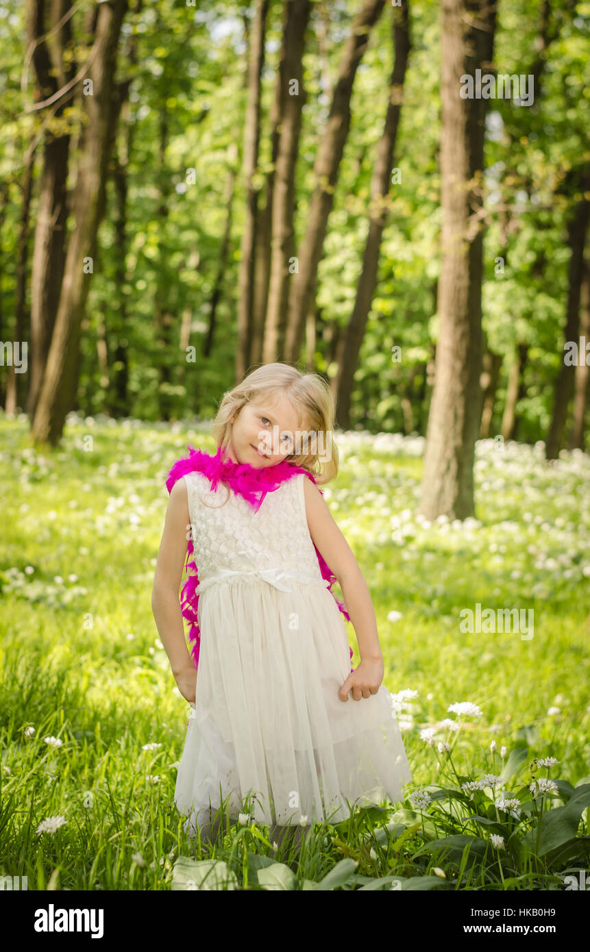 Belle petite fille blonde avec boa pourpre au printemps woods Banque D'Images