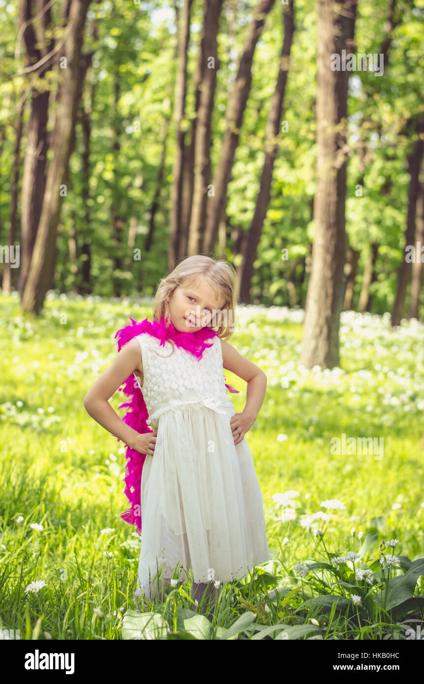 Belle petite fille blonde en robe blanche avec boa pourpre au printemps woods Banque D'Images