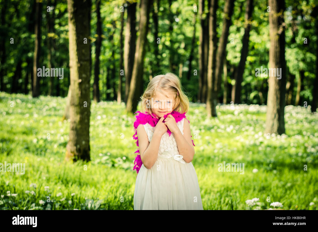 Belle petite fille blonde en robe blanche avec boa pourpre au printemps woods Banque D'Images